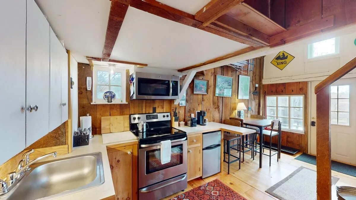 A well-lit kitchen and dining space with stainless steel appliances, wooden cabinets, a central island, and a dining area beside large windows that let in ample sunlight. The inviting setup makes it ideal for cooking, socializing, and enjoying meals with gorgeous views.