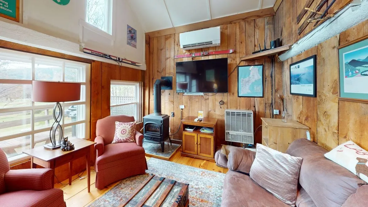 An inviting, wood-paneled living space with comfortable seating, a wood stove, decorative accents, and a TV. The room is filled with warm, ambient light and designed for cozy relaxation—perfect for curling up with a book or enjoying a movie night.