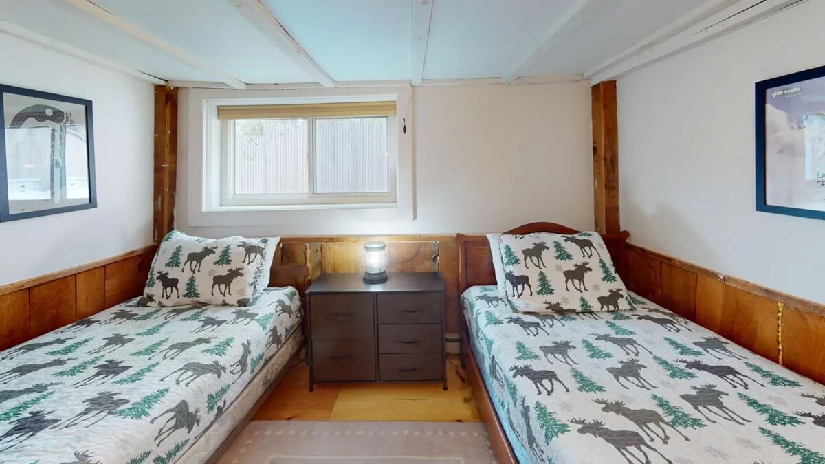 This image features two twin beds with a wooden nightstand between them, a window allowing for glimpses of the outdoors, and decorative art on the walls. The warm tones and cozy bedding evoke a sense of togetherness and relaxation, perfect for unwinding after a day of adventure.